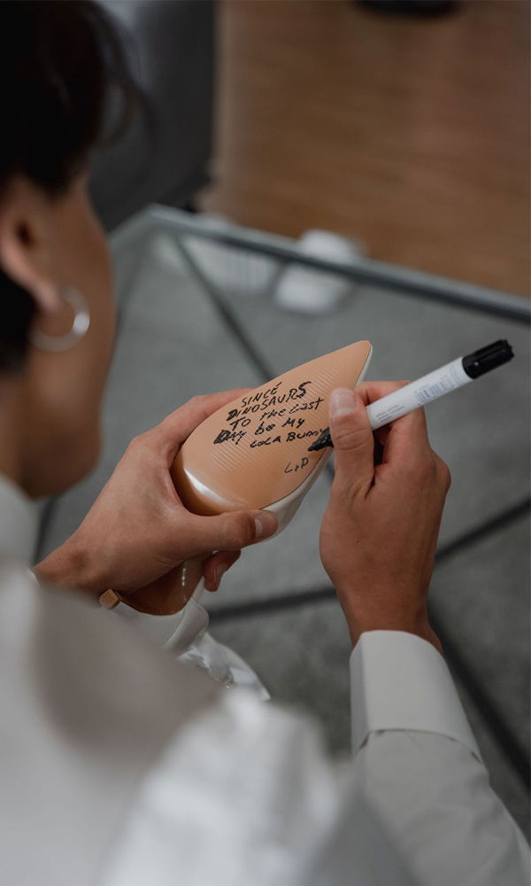 Ein Bräutigam schreibt eine romantische Botschaft auf die Sohle eines Schuhs. Das Bild zeigt eine kreative und persönliche Hochzeitsvorbereitung in einem modernen Ambiente.