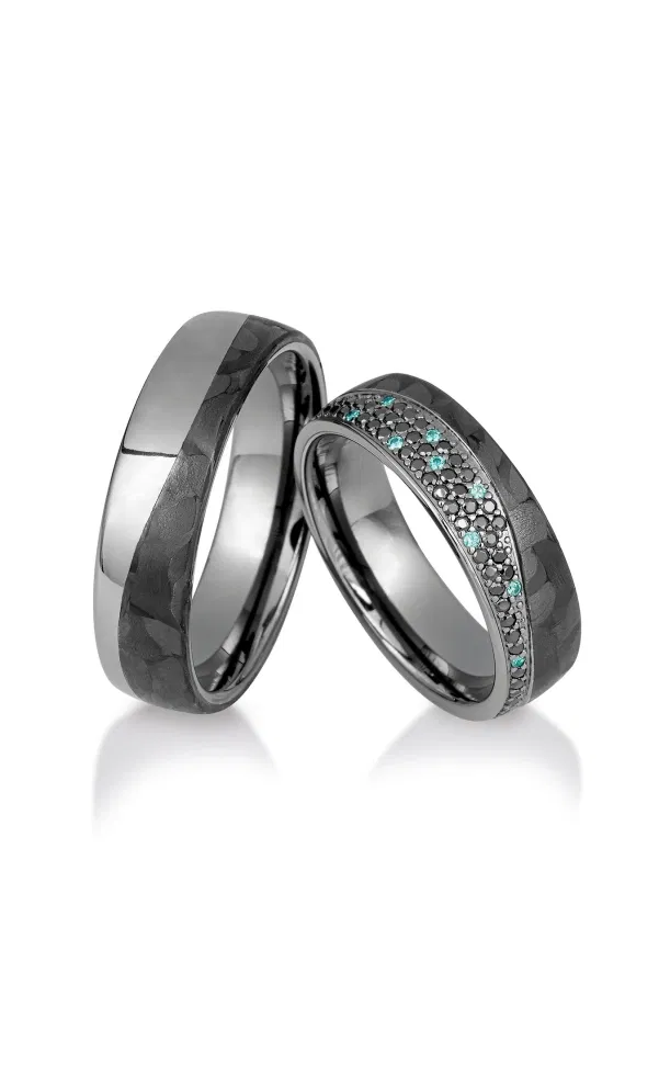 Zwei moderne Trauringe in dunklem Carbon-Design mit polierter Innenfläche; der Damenring ist mit schwarzen und türkisfarbenen Diamanten in einer Reihe besetzt.