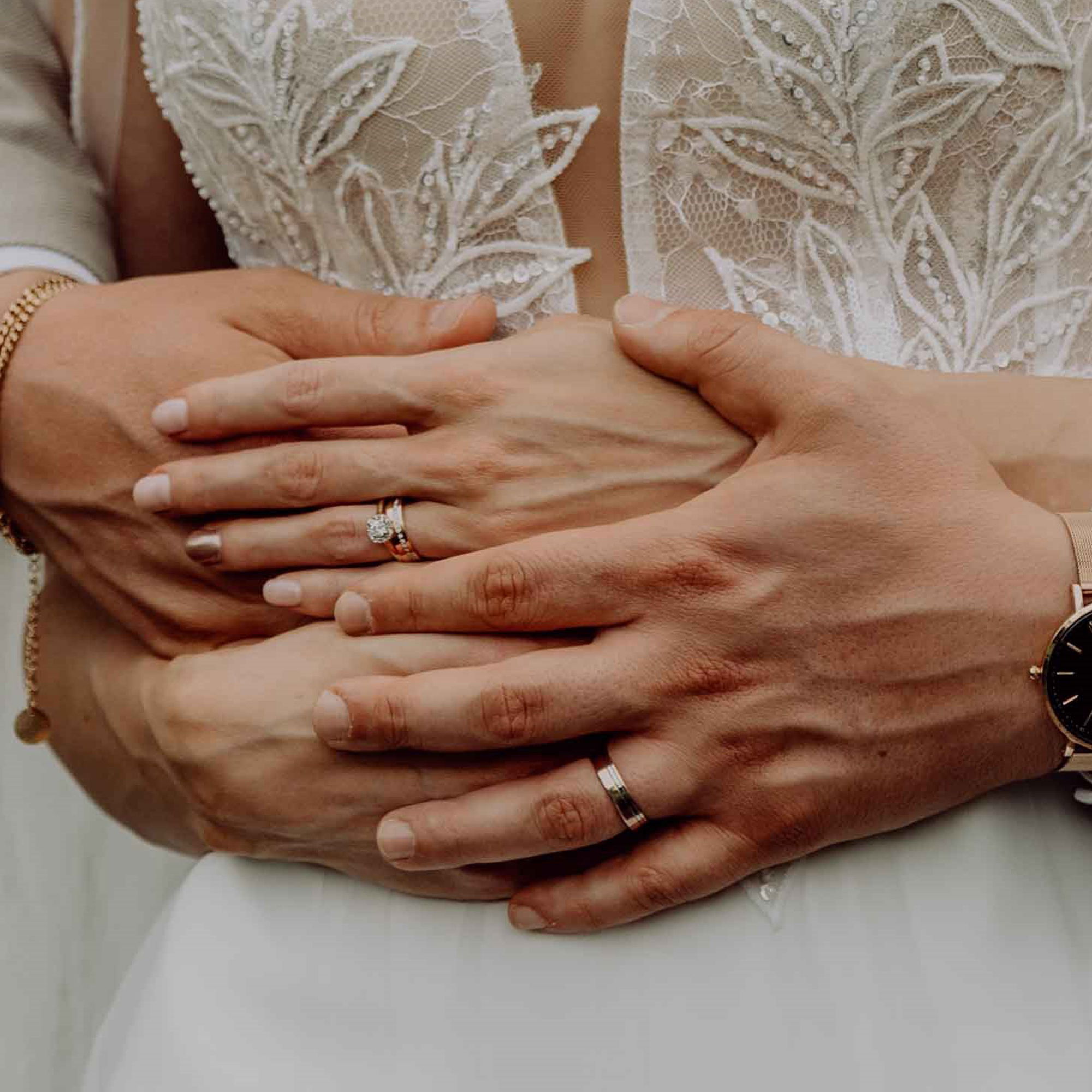 Emotionale Momentaufnahme: Die Hände eines Brautpaares mit eleganten Ringen ruhen übereinander, das Brautkleid zeigt feine Spitzenverzierungen.