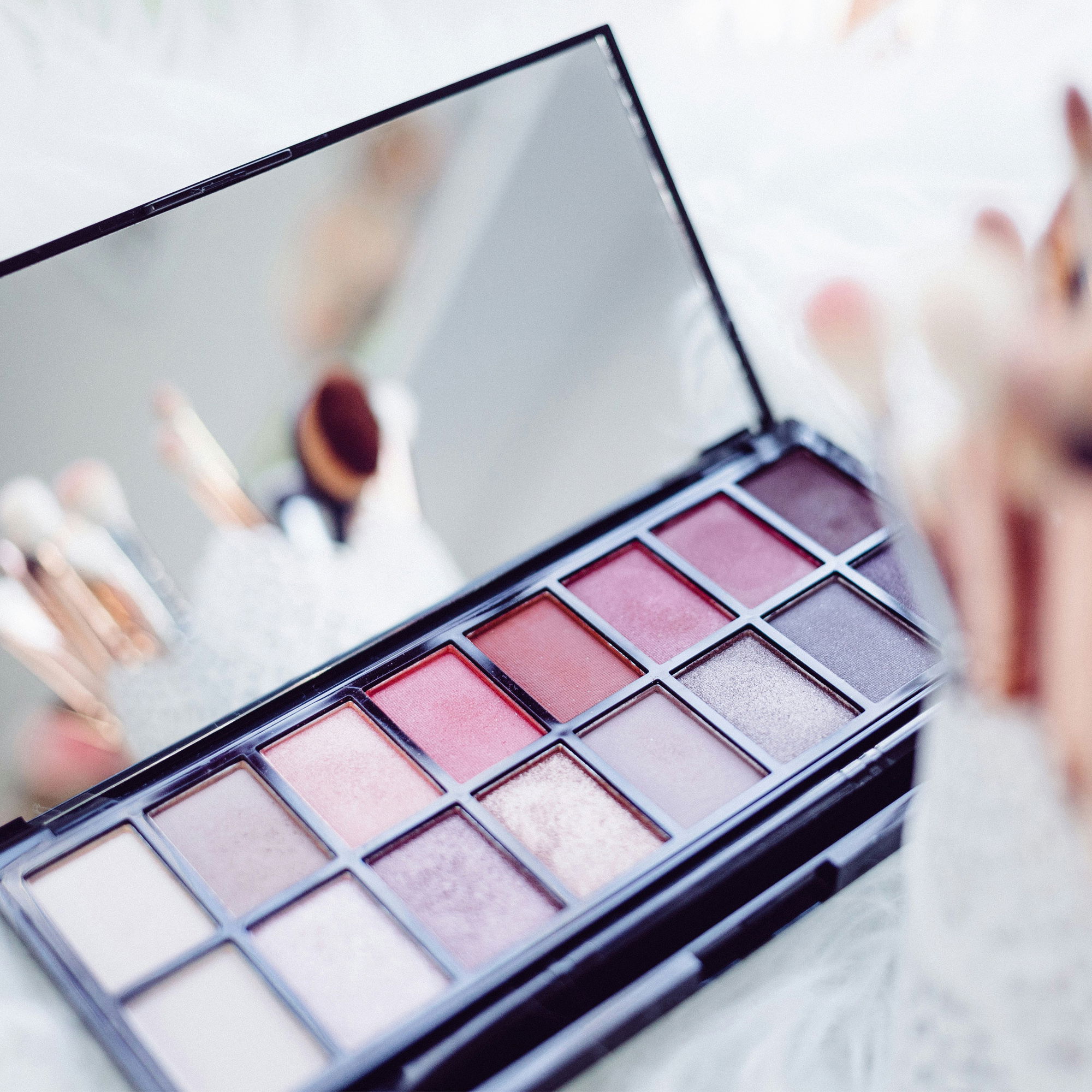 Elegante Lidschattenpalette mit schimmernden und matten Farbtönen, Spiegelreflexion zeigt Make-up-Pinsel, sanfte Ästhetik für Brautstylings.