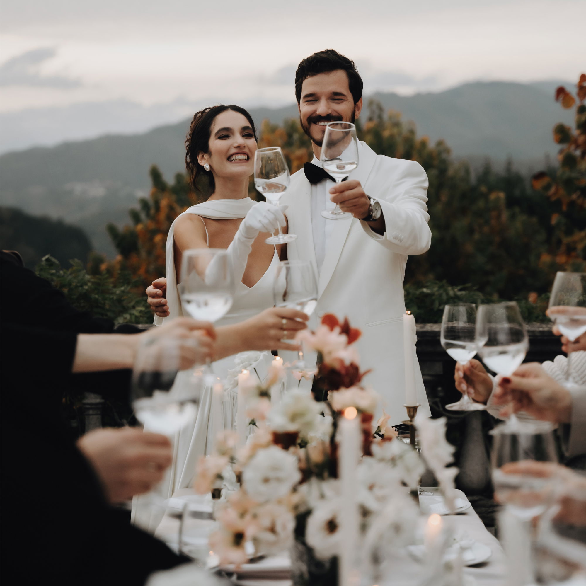 Romantischer Hochzeitsmoment: Das frisch verheiratete Paar feiert mit seinen Gästen ein festliches Dinner unter freiem Himmel mit Bergblick.