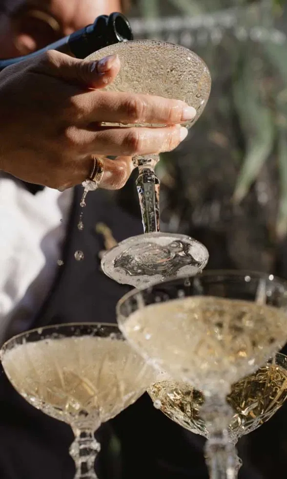 Detailaufnahme eines Champagner-Turms bei einer Hochzeit, während Champagner in Kristallgläser eingeschenkt wird.