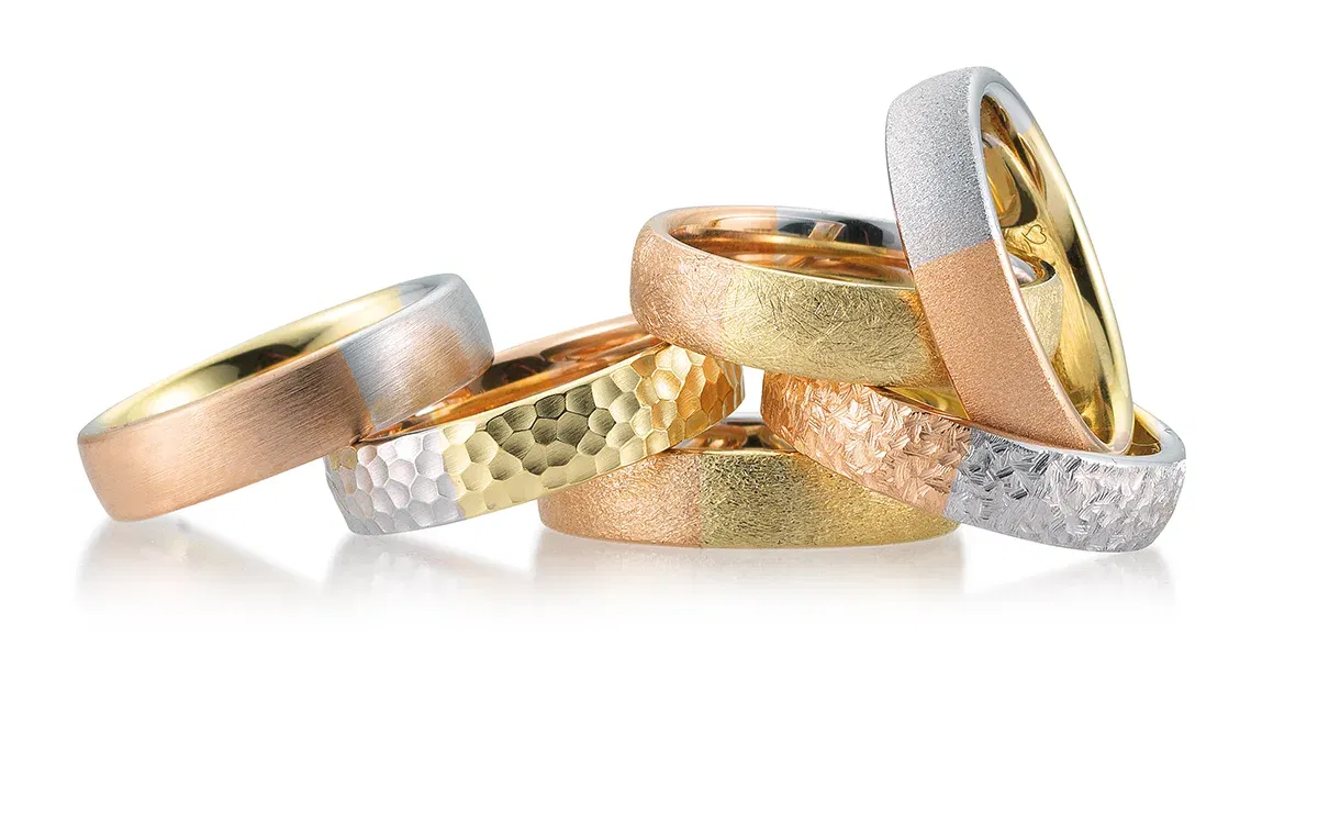 Set aus verschieden strukturierten Eheringen in Gold-, Roségold- und Silbernuancen, dekorativ übereinander gelegt.