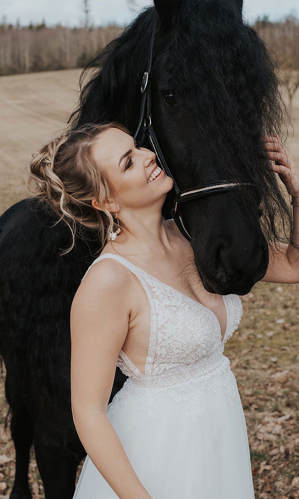 Zärtliche Umarmung zwischen Braut in Weiß und ihrem Pferd.