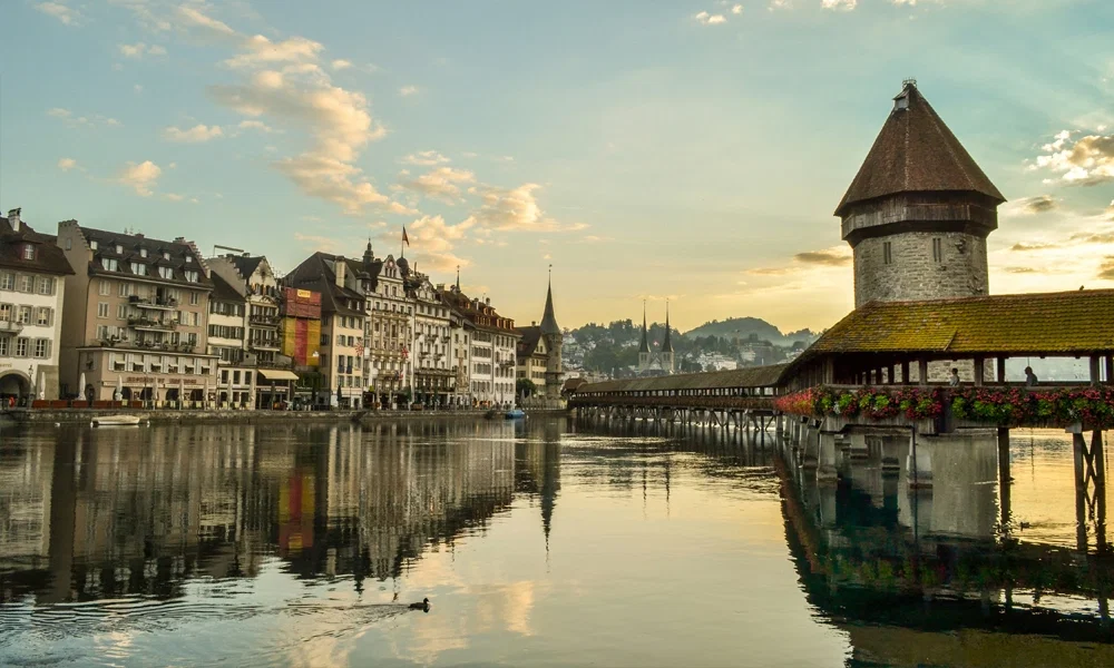 Die historische Kapellbrücke mit Wasserturm in Luzern bei Sonnenuntergang, gespiegelt im ruhigen Wasser der Reuss.