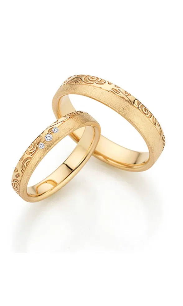 Zwei goldene Trauringe mit matter Oberfläche, feiner floraler Gravur und drei kleinen Diamanten, die das elegante Design dezent hervorheben.