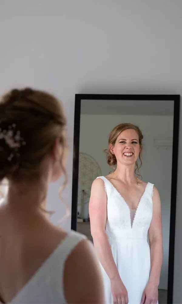 Braut betrachtet sich mit einem strahlenden Gesichtsausdruck im Spiegel, Szene in heller Umgebung.