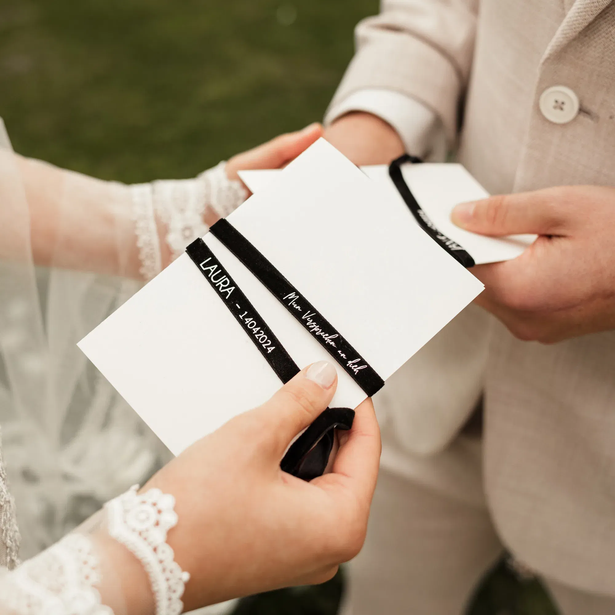 Ein Brautpaar hält jeweils eine Klappkarte mit schwarzer Banderole in den Händen und liest sich ihr Eheversprechen gegenseitig vor.