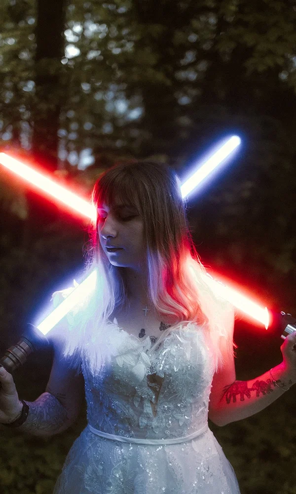 Braut mit Tattoos hält rot-blaues Laserschwert, galaktisches Hochzeitsshooting im Wald