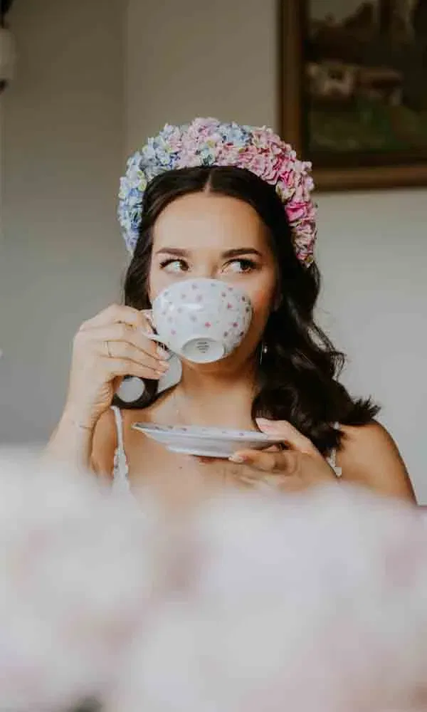Portraitaufnahme einer Frau mit floralem Kopfschmuck beim Teetrinken.