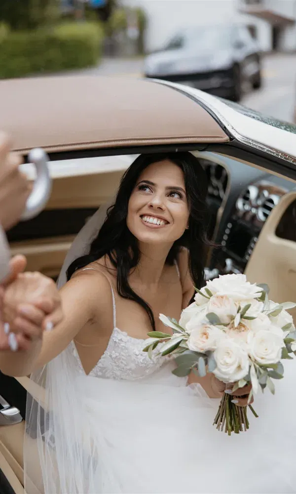 Die Braut steigt voller Vorfeude lachend aus dem Oldtimer.