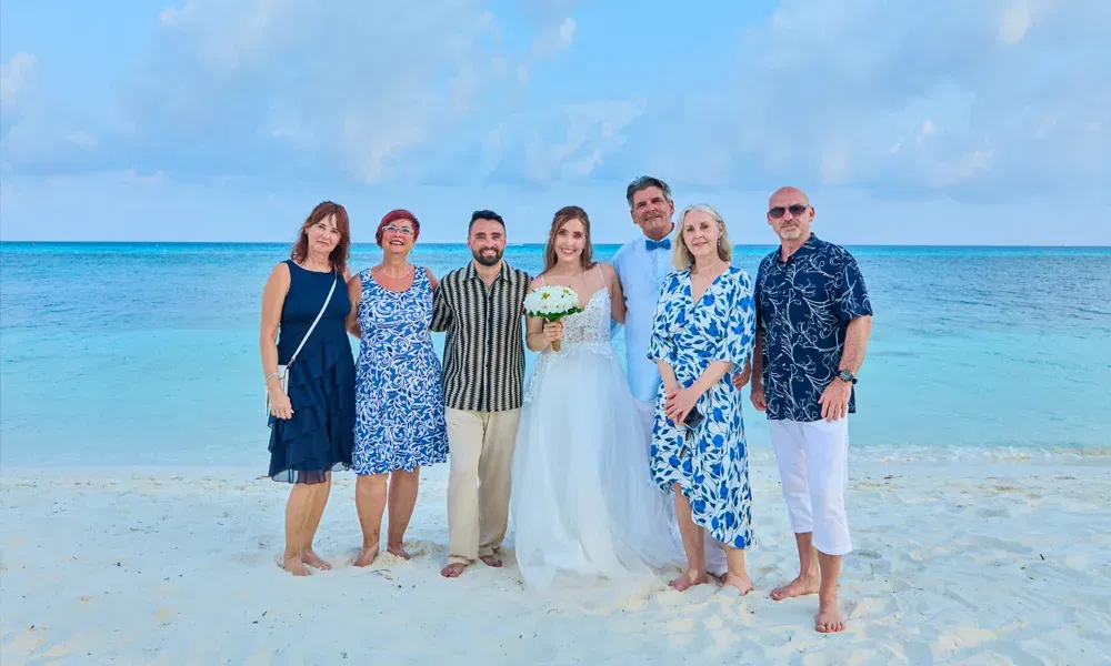 Janine und Martin mit ihren Gästen bei der intimen Hochzeit am Meer – festliches Gruppenbild vor traumhafter Meereskulisse.