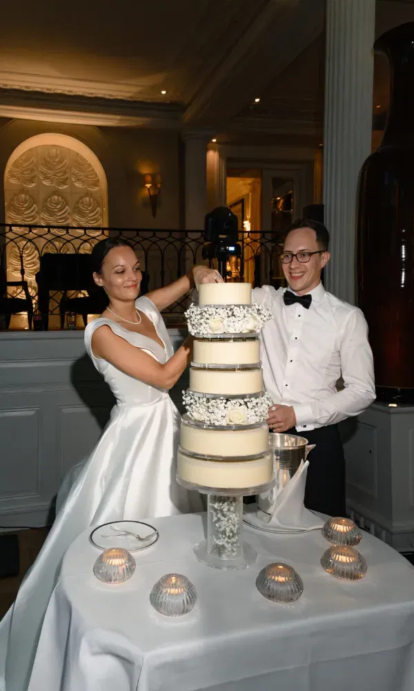 Die Hochzeitstorte wird vom Brautpaar lachend angeschnitten.