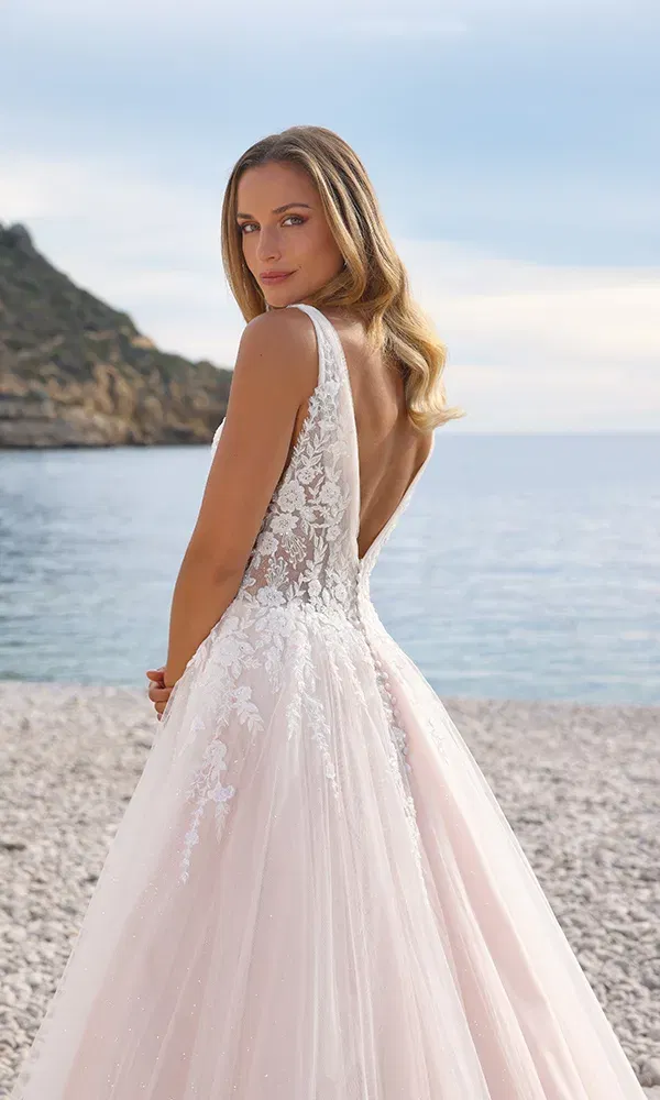 Brautkleid mit tiefem Rückenausschnitt und floraler Spitze, das mit einem fließenden Rock in Blushton für einen traumhaften Auftritt am Strand sorgt.