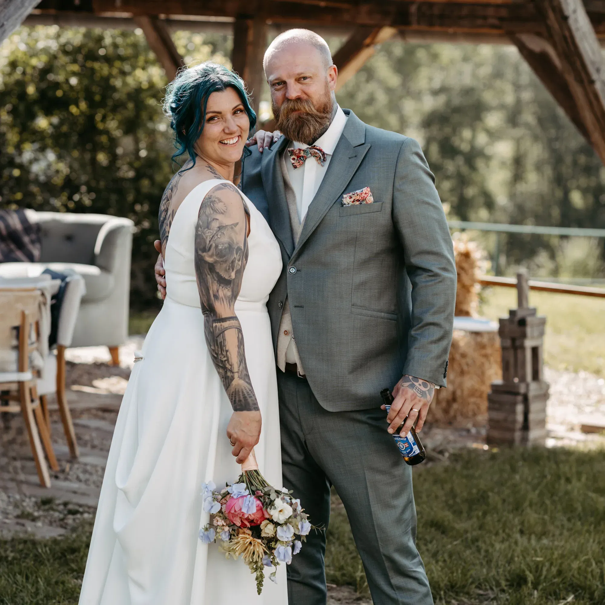 Rebeka und Florian bei ihrer freien Trauung auf dem Weingut: Sie mit Blumenstrauß und Tattoos, er leger mit Bierflasche in der Hand.