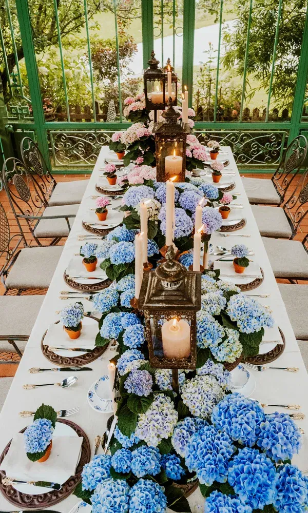 Stimmungsvolle Tischdekoration mit blauen Hortensien in Terrakottatöpfen, Vintage-Besteck und romantischen Kerzenleuchtern.