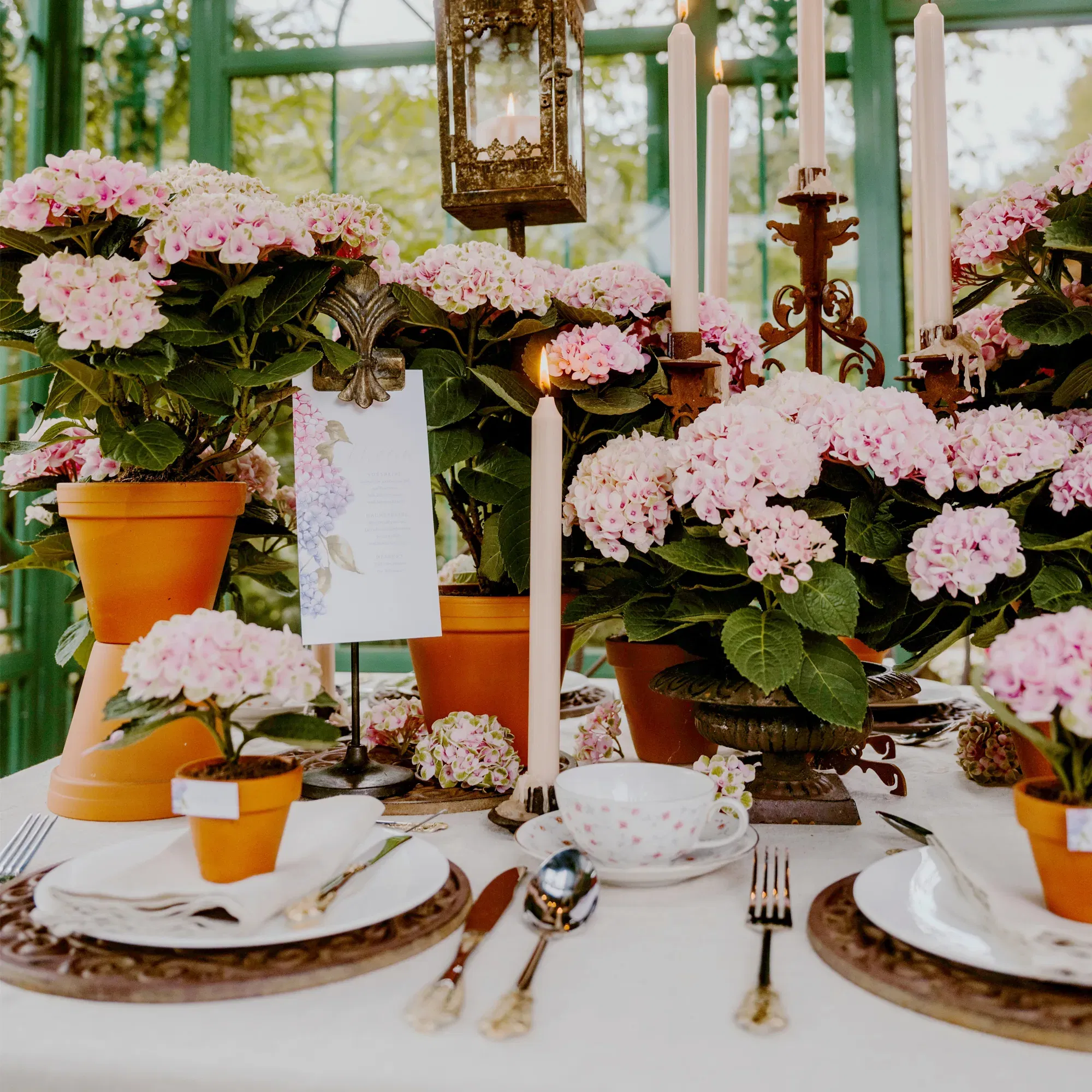 Elegante Hochzeitstafel mit rosa Blütenpracht, Menükarte, Kerzenschein und liebevoll arrangierter Blumendeko in Terrakottatöpfen.