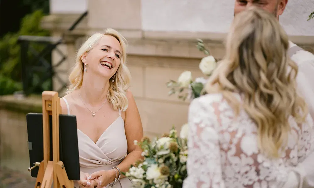 Emotionale Hochzeitsszene: Eine strahlende Rednerin spricht mit dem Brautpaar, das ihr mit Blumen und Freude begegnet.