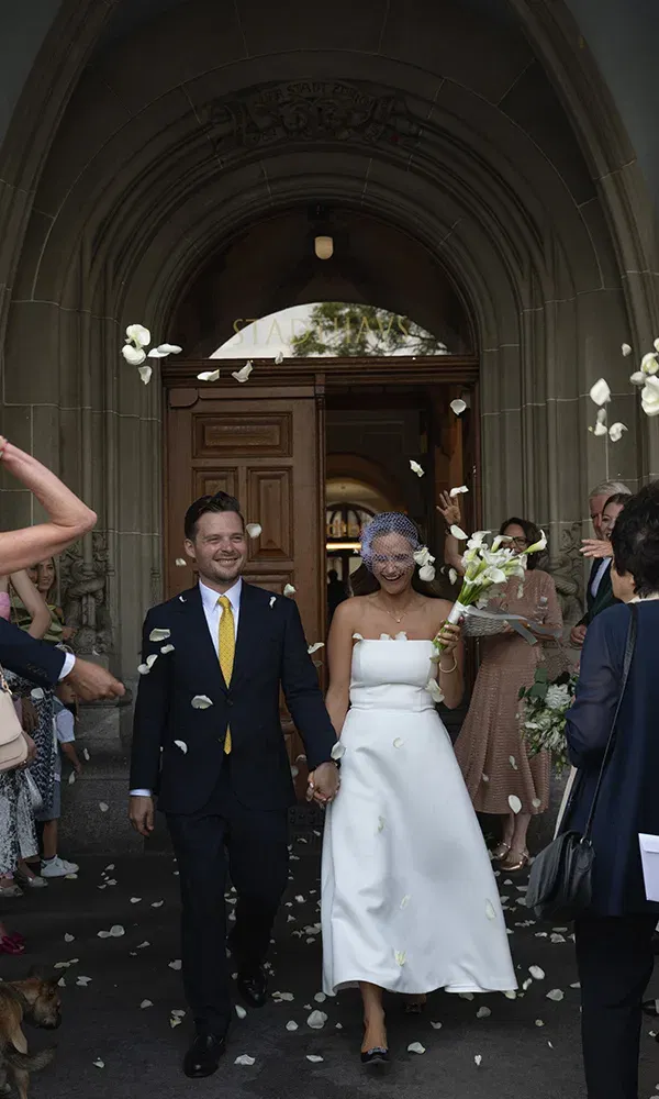 Frisch verheiratetes Paar verlässt das Standesamt in Zürich unter einem Blütenregen und strahlenden Gesichtern.