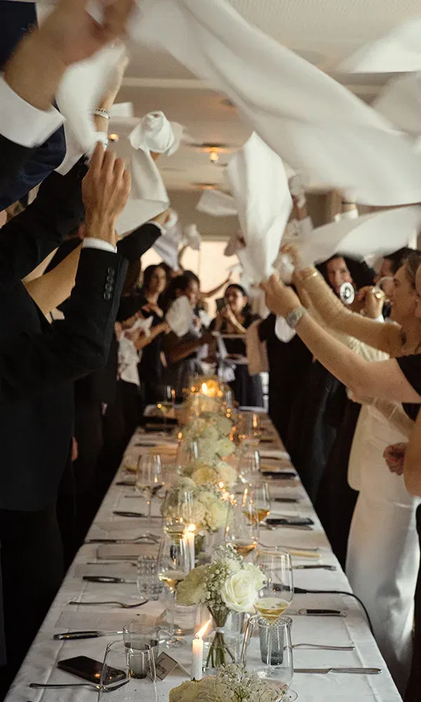 Feierliche Stimmung bei der Hochzeitstafel, Gäste schwingen Servietten über dem festlich gedeckten Tisch.