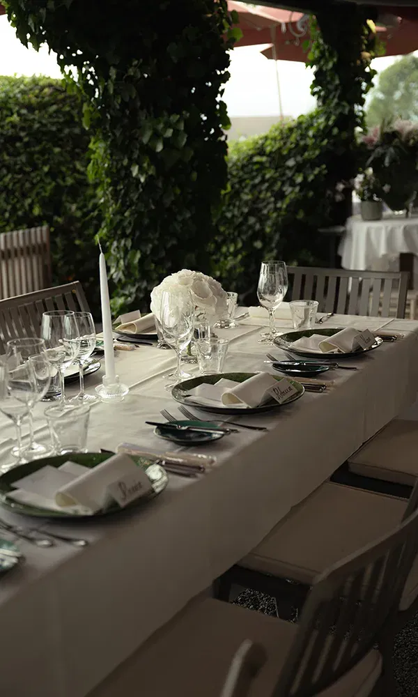 Elegant gedeckter Tisch für die Hochzeitsfeier im Freien mit weißen Blumen, Kerzen und Namenskärtchen.