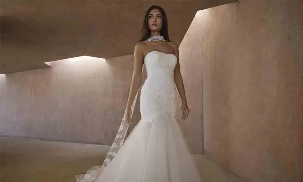 Elegante Braut in einem schulterfreien Fishtail-Kleid mit Tüllrock und zarten Spitzen-Details, fotografiert in urbaner Betonarchitektur.