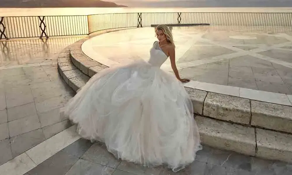 Romantische Szene: Frau im Prinzessinnenkleid mit asymmetrischem Oberteil sitzt entspannt vor weiter Meereskulisse im sanften Licht der Dämmerung.