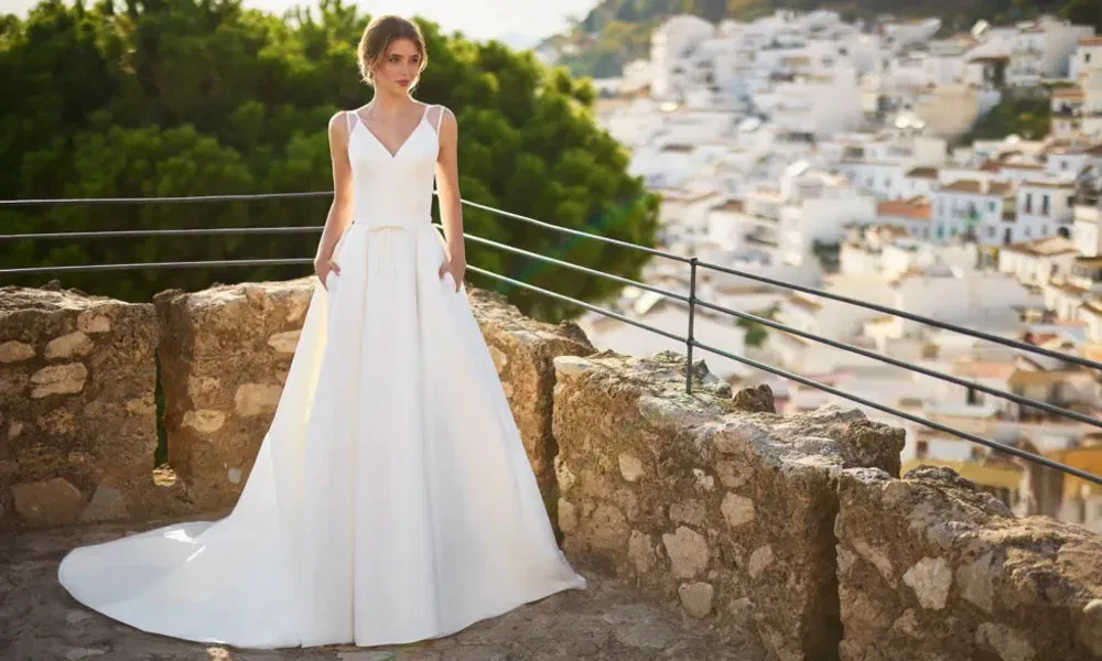 Modernes A-Linien-Kleid mit schmalem Taillengürtel und tiefem Ausschnitt – Braut vor südländischer Kulisse auf einer historischen Aussichtsplattform.