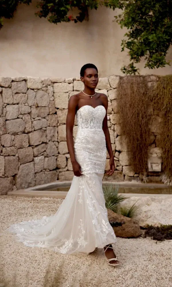 Gesamtaufnahme einer Braut im Fit-and-Flare-Kleid mit langer Schleppe vor rustikaler Kulisse aus Steinen und Trockenpflanzen.