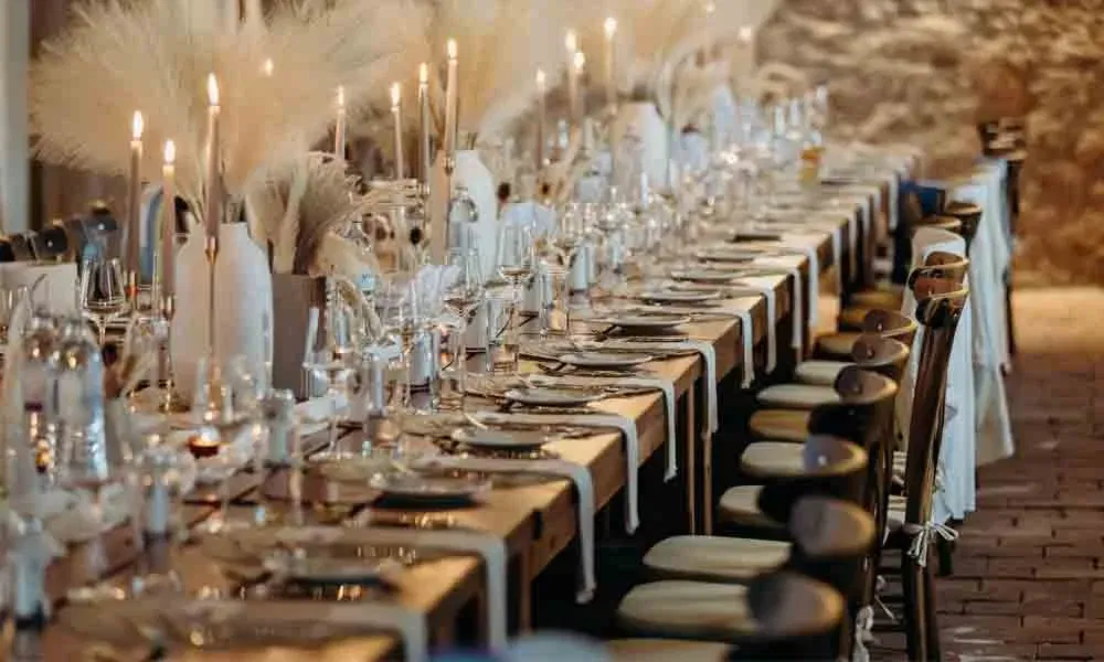 Detailreiche Hochzeitsdeko: lange Tafel mit edler Boho-Dekoration, hohen Kerzenhaltern und Naturmaterialien auf Holztischen.