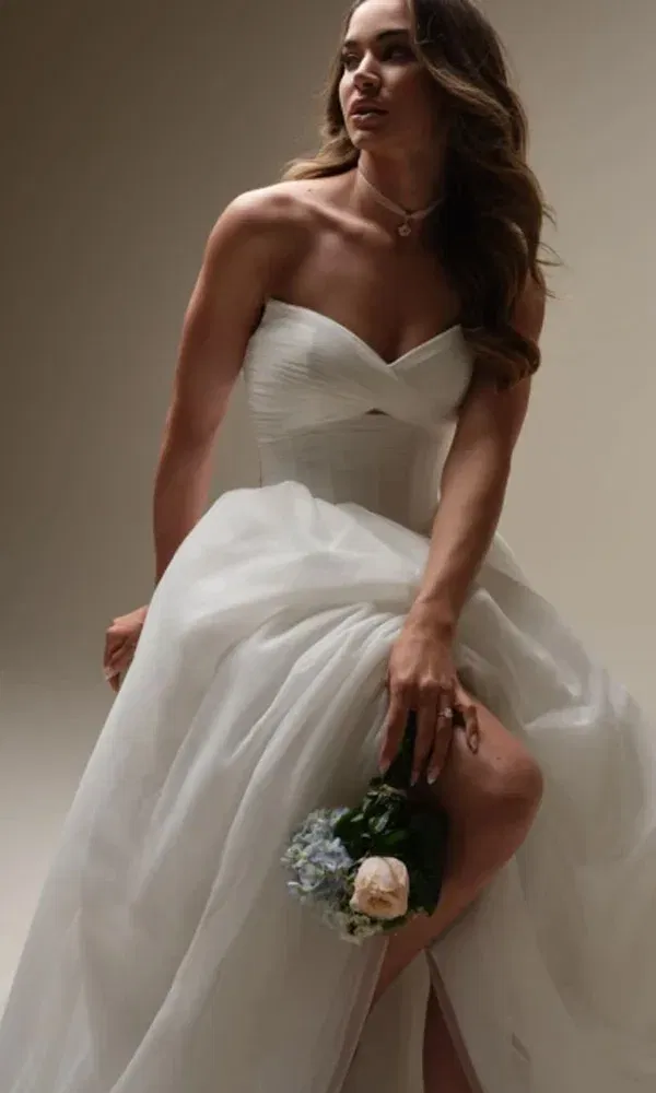 Sinnliches Hochzeitsfoto einer Braut im luftigen Kleid mit Beinschlitz, die einen Strauß aus Hortensien und Rose hält.