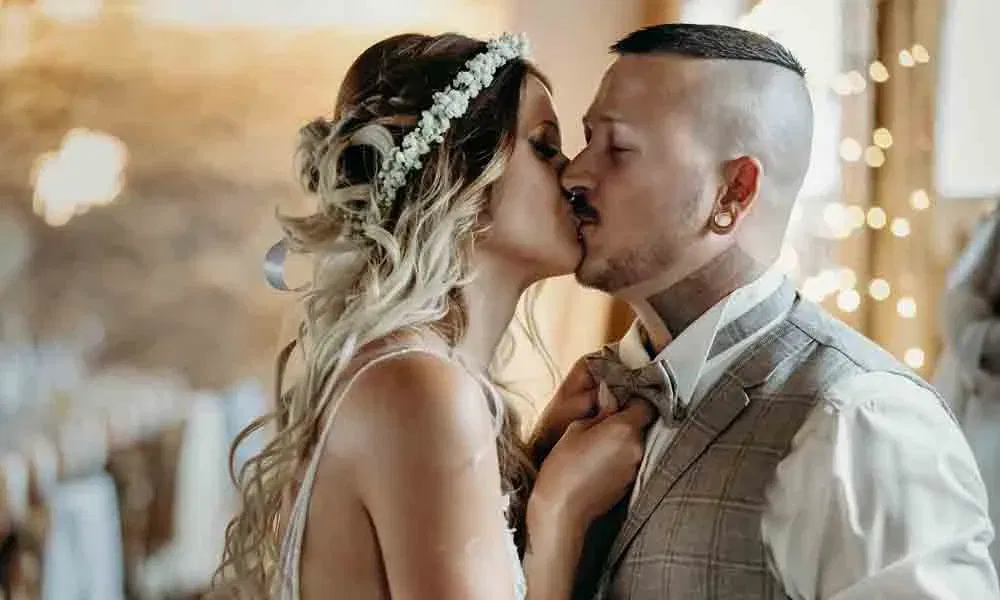 Zärtliche Hochzeitsaufnahme: Die Braut zieht den Bräutigam sanft an sich, während Lichter im Hintergrund für warme Stimmung sorgen.