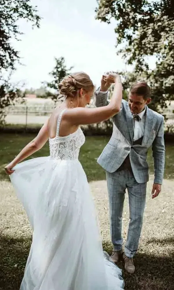 Das Brautpaar dreht sich beim Hochzeitstanz auf dem Rasen – sie in Spitze, er im karierten Anzug.