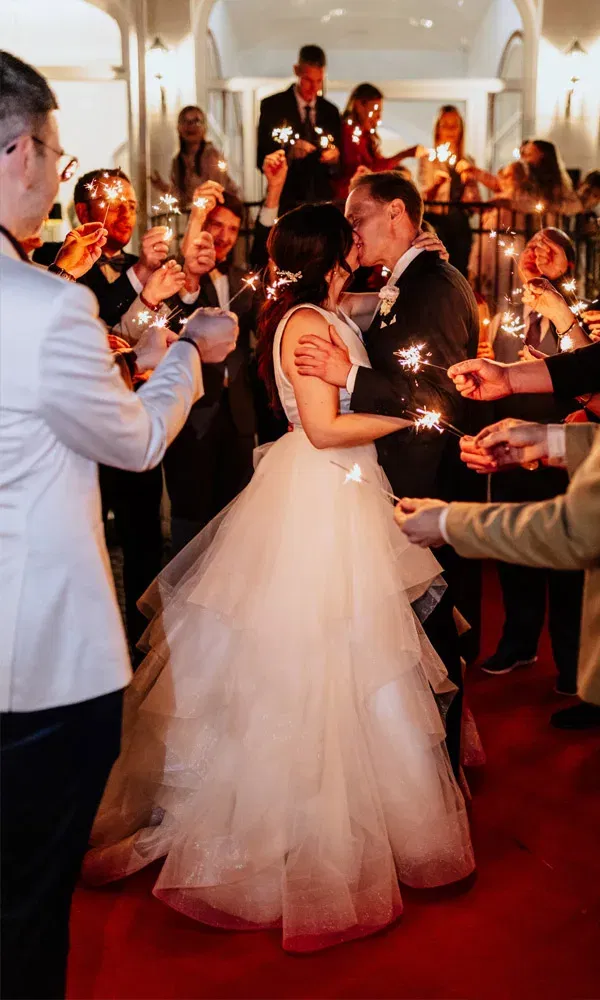 Romantischer Hochzeitsmoment mit dem Brautpaar inmitten von jubelnden Gästen und leuchtenden Wunderkerzen.