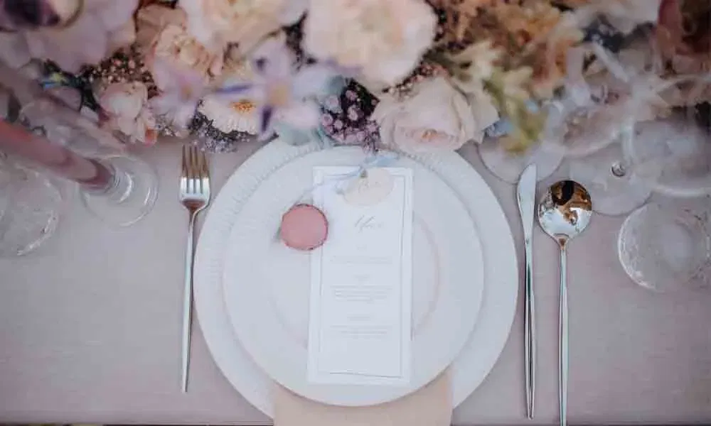 Detailaufnahme eines edel gedeckten Hochzeitstellers mit Menükarte, pinkem Macaron und romantischer Blumendeko in Pastellfarben.