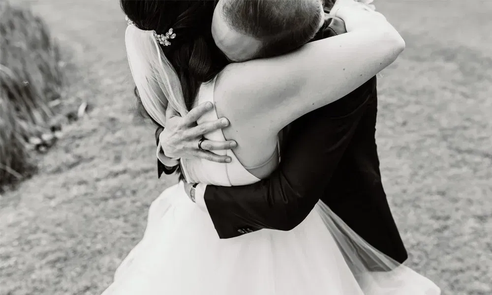 Bräutigam umarmt seine Braut mit geschlossenen Augen, die Szene wirkt vertraut und intensiv, monochrom fotografiert.
