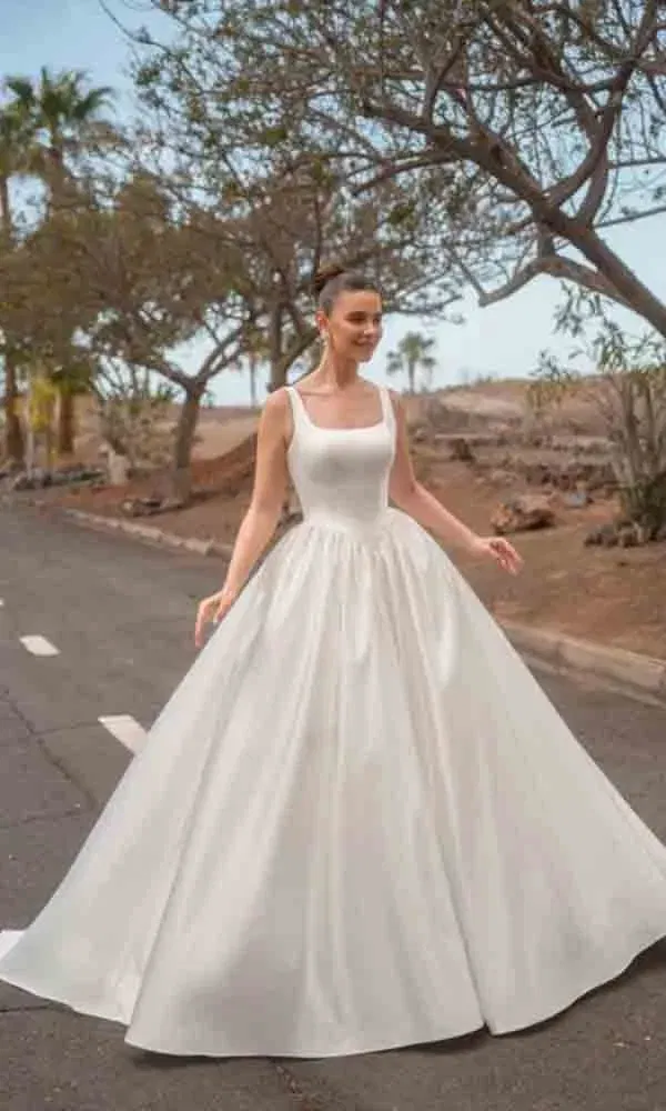 Natürlicher Brautmoment: Frau im klassischen Brautkleid mit Square-Neck auf einer Straße mit Palmen und Bäumen.