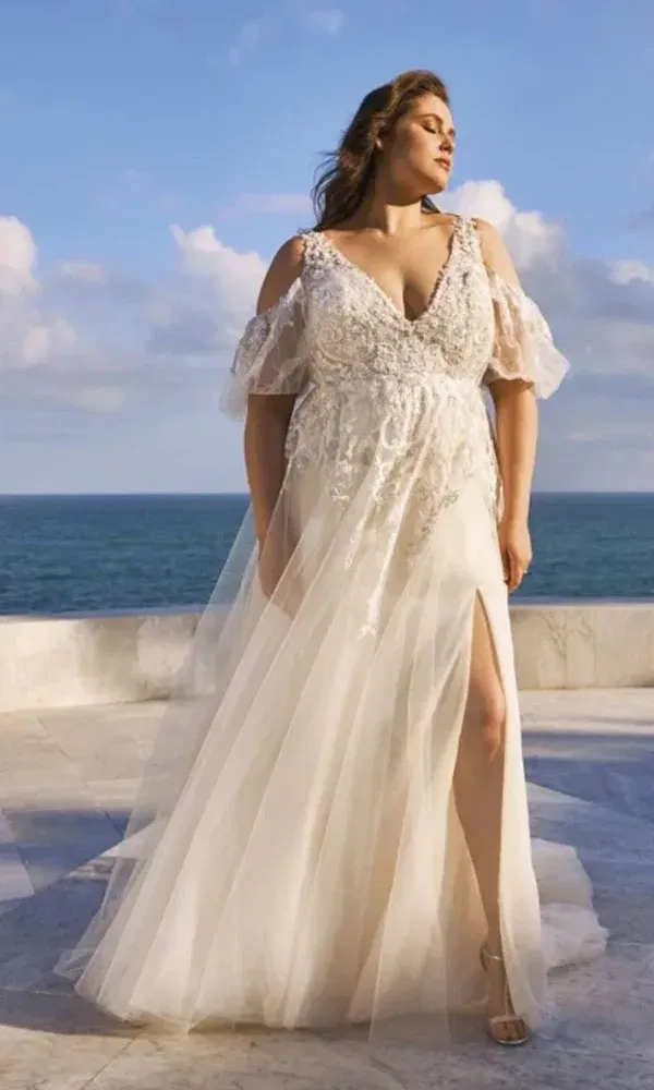 Braut mit Plus-Size-Figur zeigt sich in einem romantischen Boho-Kleid mit verspielten Ärmeln und Meerblick.
