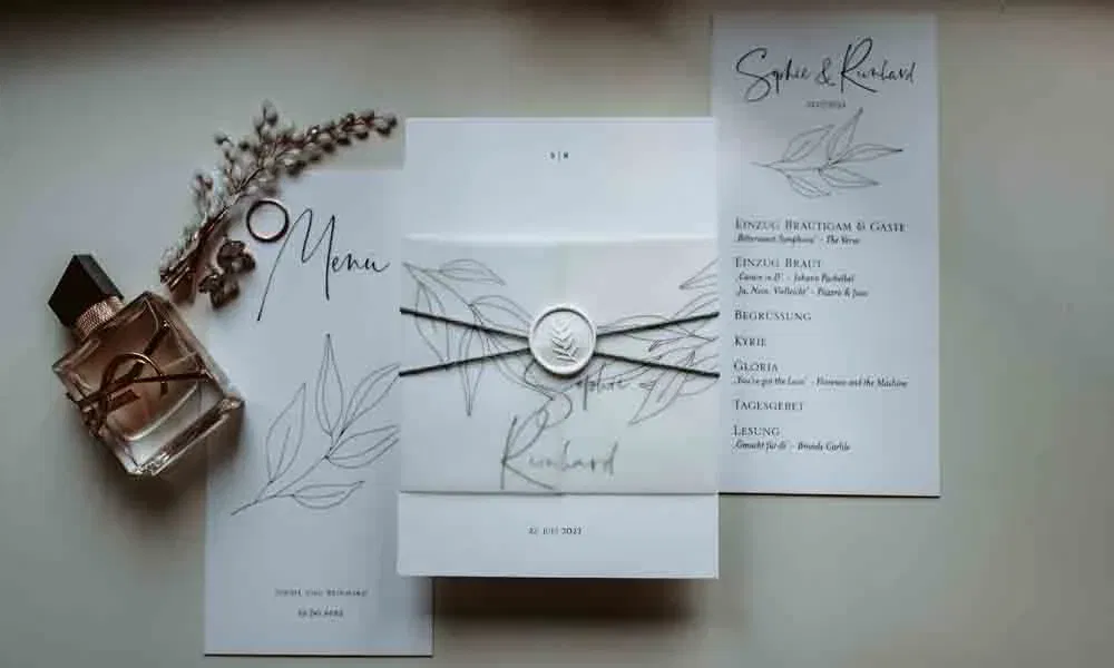 Einladungsset von Sophie & Reinhard im botanischen Stil mit zarter Kalligraphie, Siegelband und Accessoires wie Parfum und Deko.
