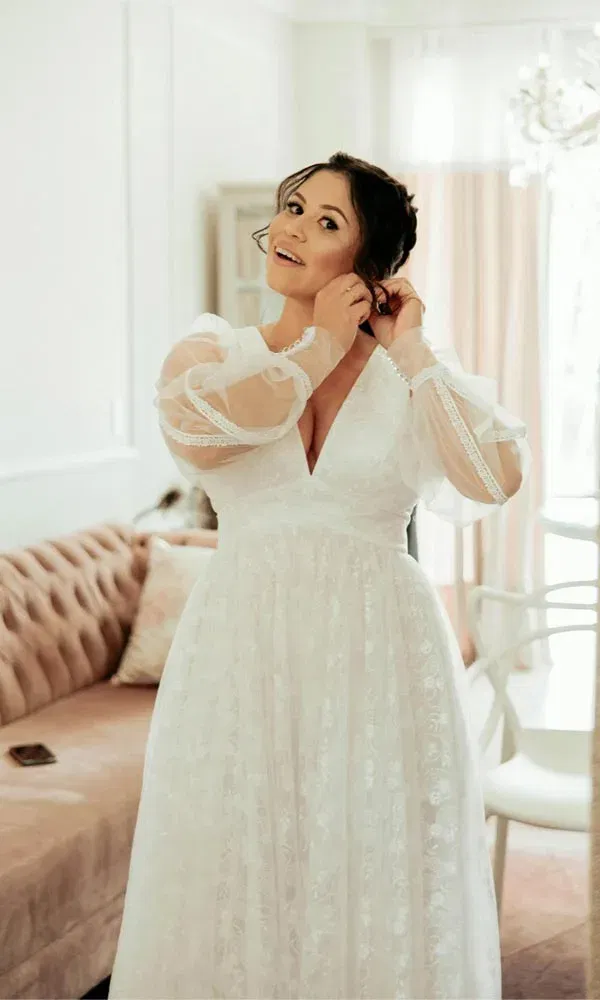 Lächelnde Braut stylt sich im Ankleidezimmer mit zarten Tüllärmeln und elegantem Kleid.