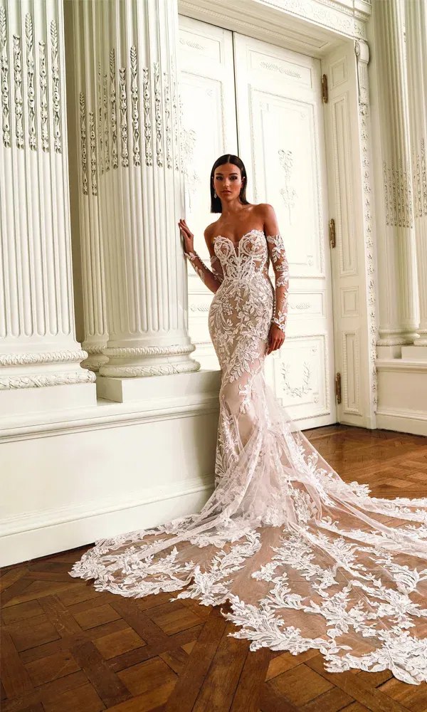 Model in einem glamourösen, trägerlosen Fit-and-Flare-Brautkleid mit illusionärer Spitze und ausladender Schleppe, posierend vor detailreichen weißen Türen und Säulen in einem herrschaftlichen Raum.