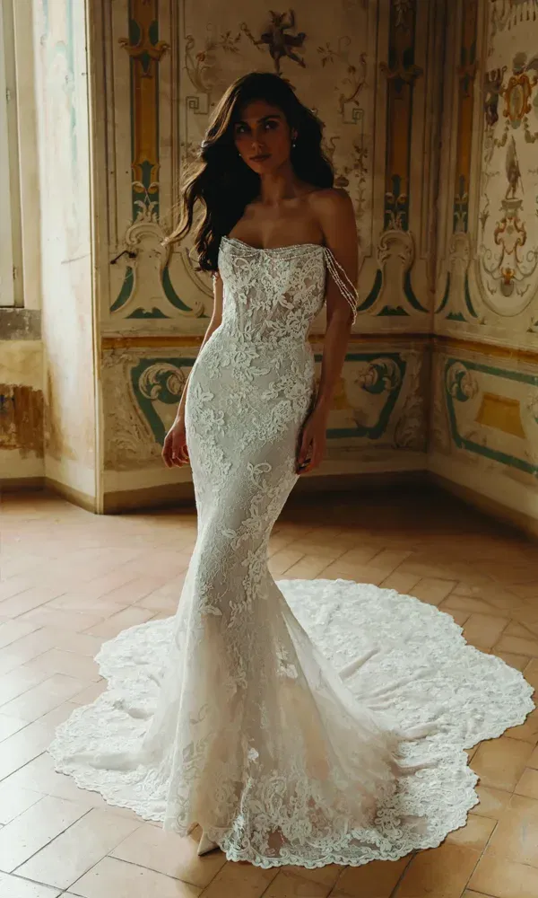 Model in einem romantischen Fit-and-Flare-Brautkleid mit feinen Stickereien und dramatischer Schleppe, fotografiert in einem Raum mit barocker Wanddekoration und Altbauflair.