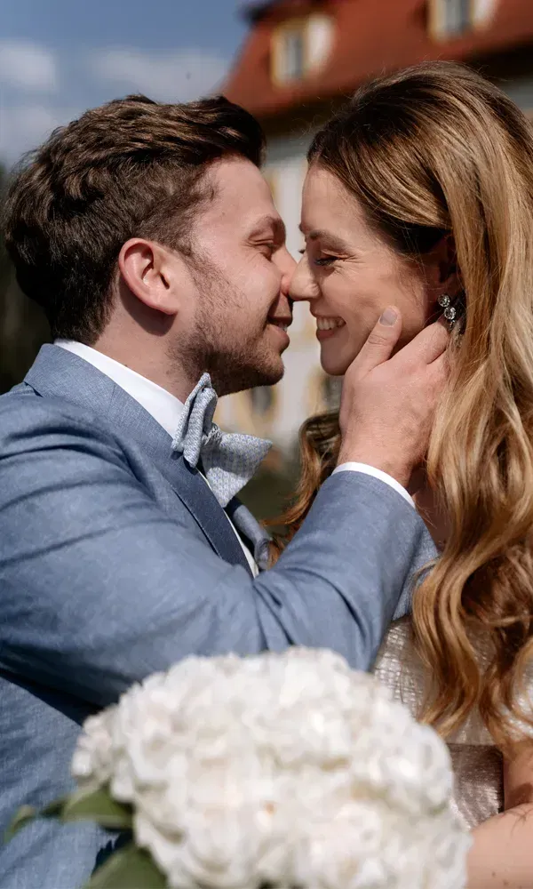 Verliebter Blickaustausch bei der Hochzeit: Das Paar berührt sich sanft an der Stirn, Braut mit offenen Haaren und weißem Brautstrauß.