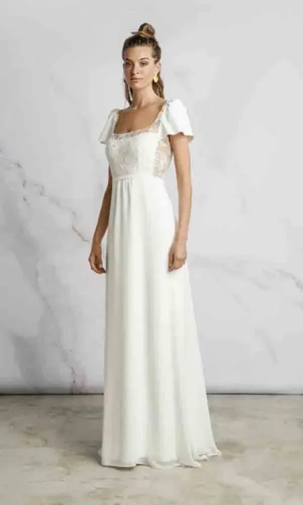 Feminines Empire-Kleid mit romantischen Details wie Flügelärmeln und transparentem Spitzeneinsatz, elegant präsentiert im Porträtformat.