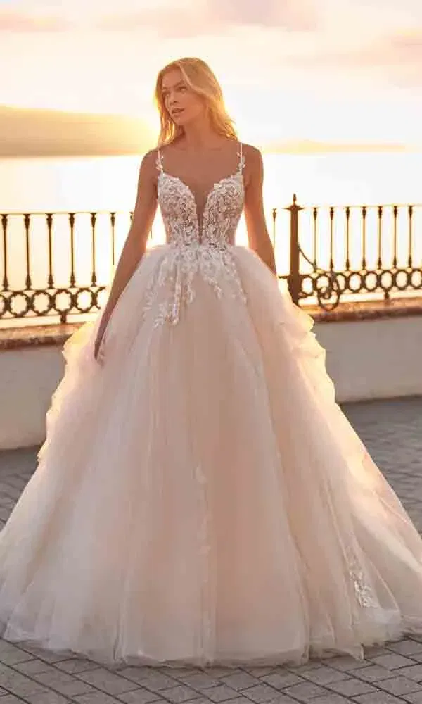 Romantischer Brautmoment: Figurbetontes Brautkleid mit Blütendetails und Spaghettiträgern in der Abendsonne am Wasser.