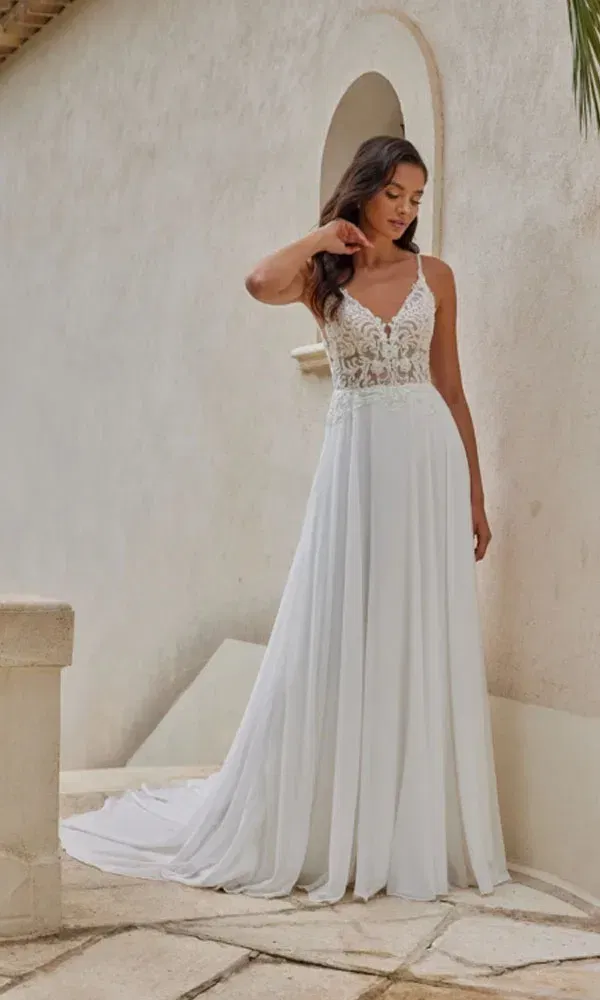 Romantische Braut in einem eleganten Kleid mit Spitzenmieder und weich fallendem Rock auf hellem Natursteinboden.