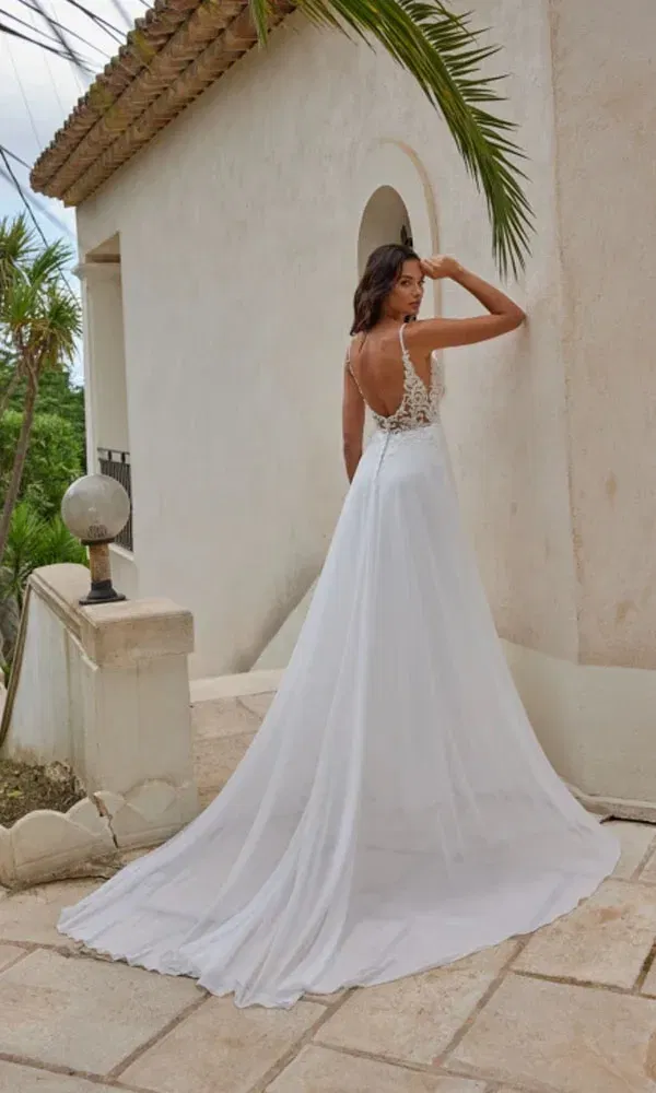 Zarte Brautsilhouette mit transparenter Spitze und langer Schleppe in einem sommerlichen Ambiente unter Palmen.