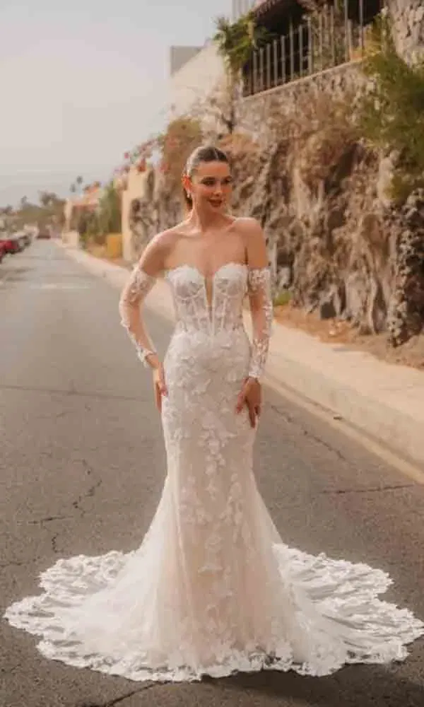 Figurbetontes Brautkleid mit transparenter Corsage und Spitzenärmeln, inszeniert im urbanen Outdoor-Setting.