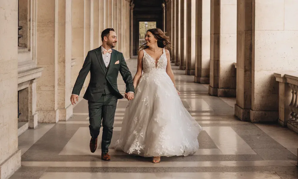 Paar in Hochzeitskleidung spaziert verliebt durch eine Säulenhalle – romantisches After-Wedding-Shooting in Paris.