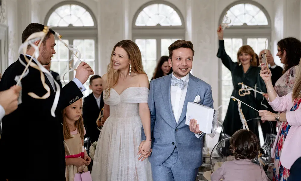 Feierlicher Einzug des Brautpaares in heller, lichtdurchfluteter Umgebung – Gäste jubeln und wedeln mit goldenen Schleifen.